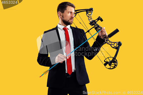 Image of Businessman aiming at target with bow and arrow, isolated on yellow background