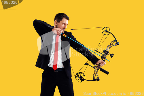 Image of Businessman aiming at target with bow and arrow, isolated on yellow background