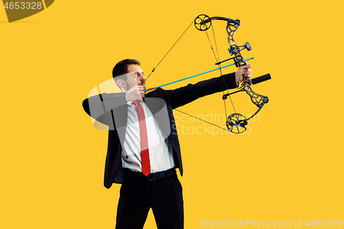 Image of Businessman aiming at target with bow and arrow, isolated on yellow background