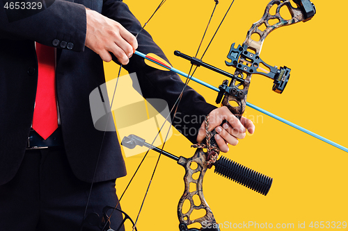 Image of Businessman aiming at target with bow and arrow, isolated on yellow background