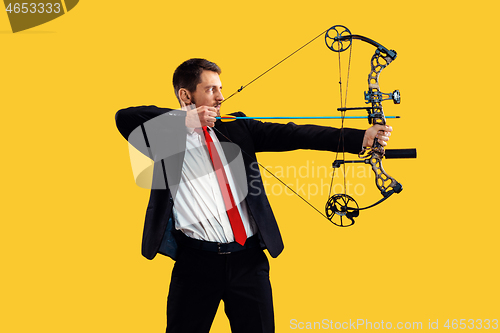 Image of Businessman aiming at target with bow and arrow, isolated on yellow background