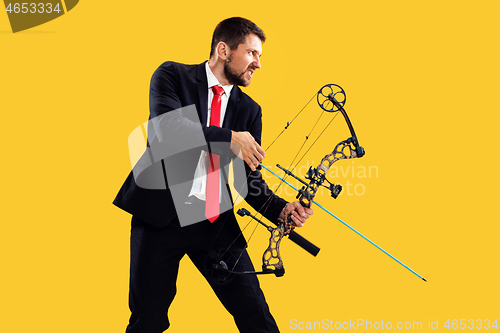 Image of Businessman aiming at target with bow and arrow, isolated on yellow background