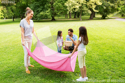 Image of family laying down picnic blanket in summer park