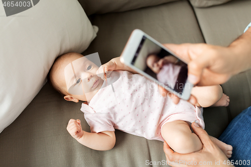 Image of father with smartphone taking picture baby at home