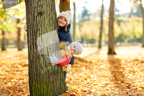 Image of happy children peeking out tree at autumn park