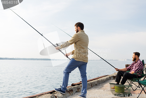 Image of male friends with fishing rods on sea pier