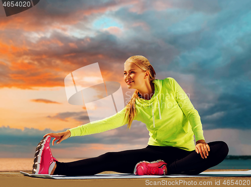 Image of woman stretching on exercise mat at seaside