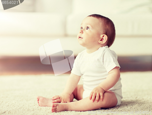 Image of happy baby boy or girl sitting on floor at home