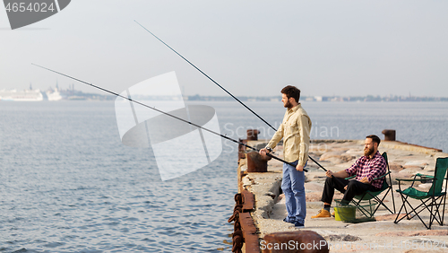 Image of male friends with fishing rods on sea pier