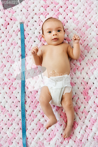 Image of baby girl lying with measure tape on blanket