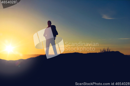Image of traveller standing on edge of hill over sunrise