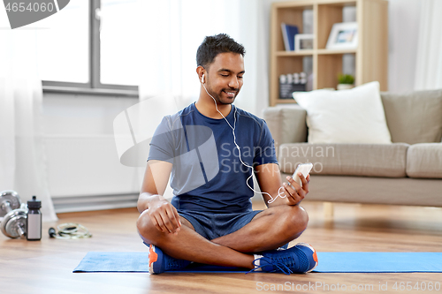 Image of indian man with smartphone on exercise mat at home