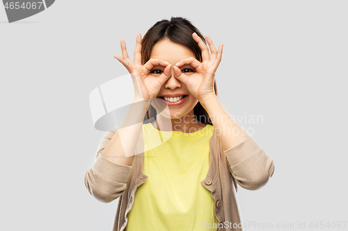 Image of smiling asian woman looking through finger glasses