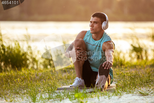 Image of A young athletic man working out listening to the music at the riverside outdoors