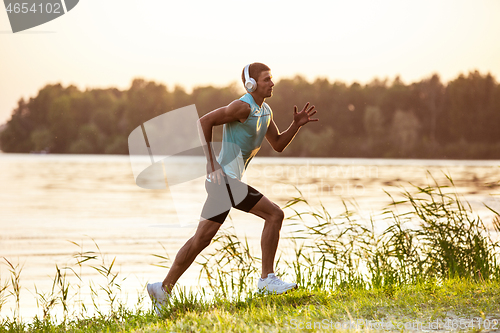 Image of A young athletic man working out listening to the music at the riverside outdoors