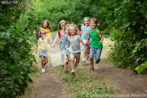 Image of Kids, children running on green meadow, forest. Childhood and summertime