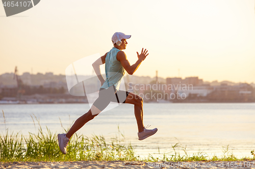 Image of A young athletic man working out listening to the music at the riverside outdoors