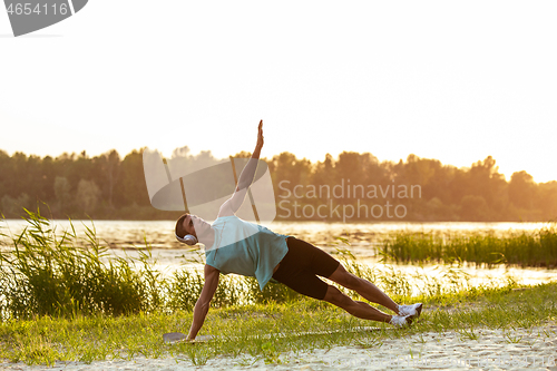 Image of A young athletic man working out listening to the music at the riverside outdoors