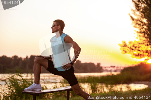 Image of A young athletic man working out listening to the music at the riverside outdoors