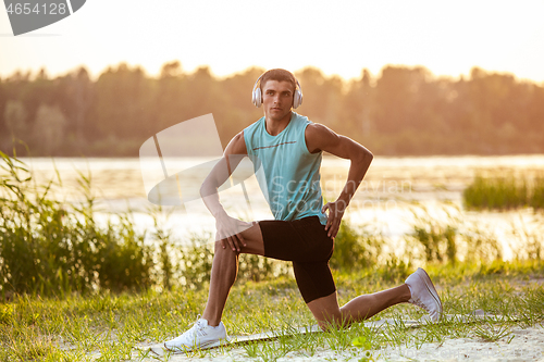 Image of A young athletic man working out listening to the music at the riverside outdoors