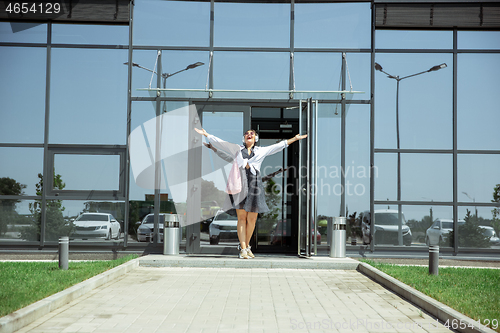 Image of Young woman walking against glass\' wall in airport, traveler with small baggage, influencer\'s lifestyle