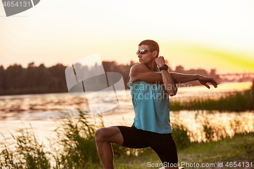 Image of A young athletic man working out listening to the music at the riverside outdoors