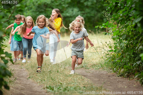 Image of Kids, children running on green meadow, forest. Childhood and summertime