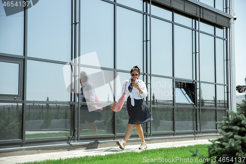 Image of Young woman walking against glass\' wall in airport, traveler with small baggage, influencer\'s lifestyle