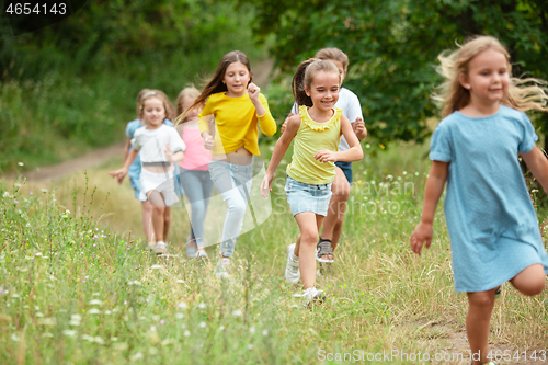 Image of Kids, children running on green meadow, forest. Childhood and summertime