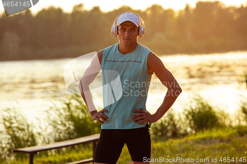 Image of A young athletic man working out listening to the music at the riverside outdoors