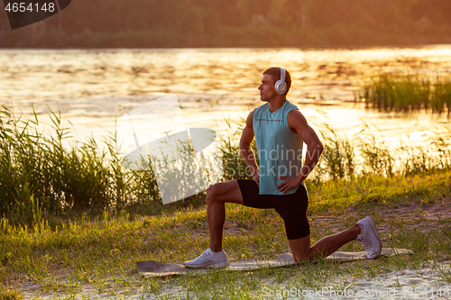 Image of A young athletic man working out listening to the music at the riverside outdoors