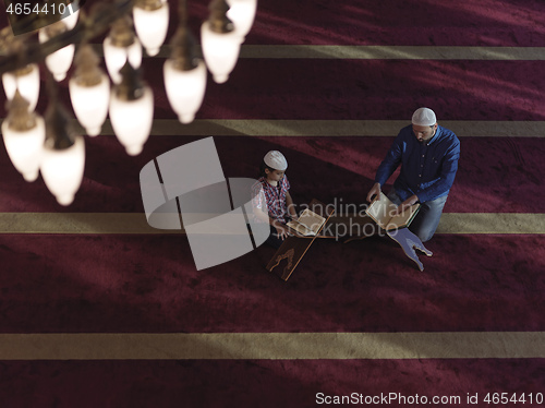 Image of father and son in mosque praying and reading holly book quran to