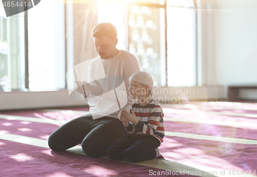 Image of father and son in mosque praying and reading holly book quran to