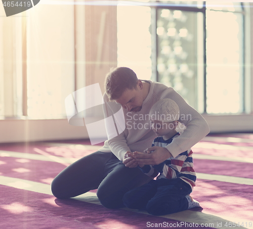 Image of father and son in mosque praying and reading holly book quran to