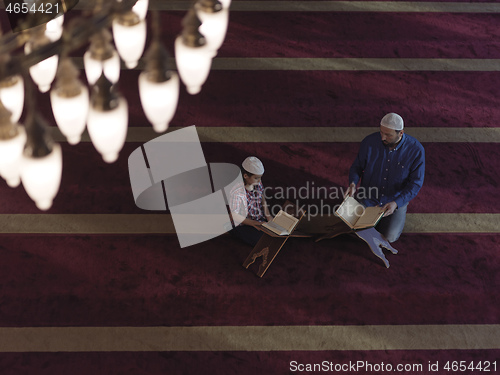 Image of father and son in mosque praying and reading holly book quran to