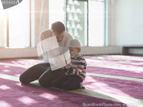 Image of father and son in mosque praying and reading holly book quran to