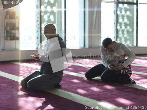 Image of father and son in mosque praying and reading holly book quran to