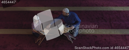 Image of father and son in mosque praying and reading holly book quran to