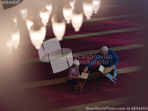 Image of father and son in mosque praying and reading holly book quran to