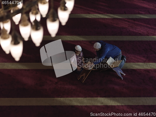 Image of father and son in mosque praying and reading holly book quran to