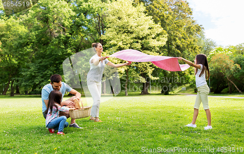 Image of family laying down picnic blanket in summer park