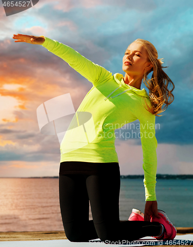 Image of woman stretching on exercise mat over sea sunset