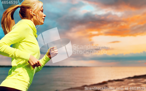 Image of woman with earphones running over sea sunset