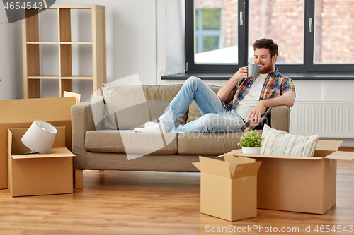 Image of man with boxes and drinking coffee at new home