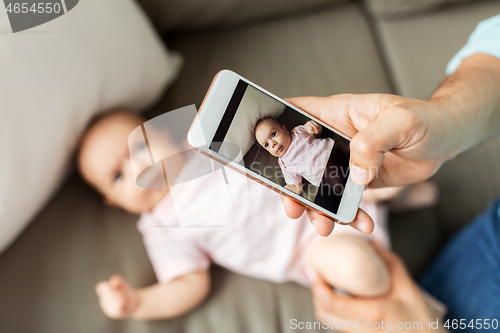 Image of father with smartphone taking picture baby at home