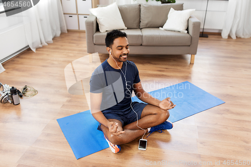 Image of indian man meditating in lotus pose at home