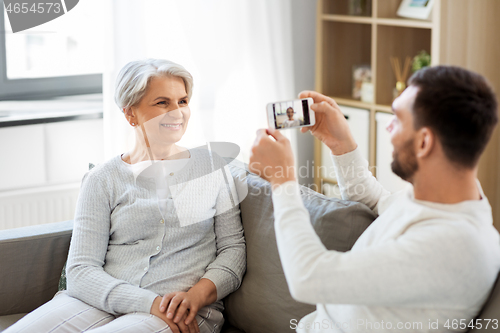 Image of adult son photographing senior mother at home