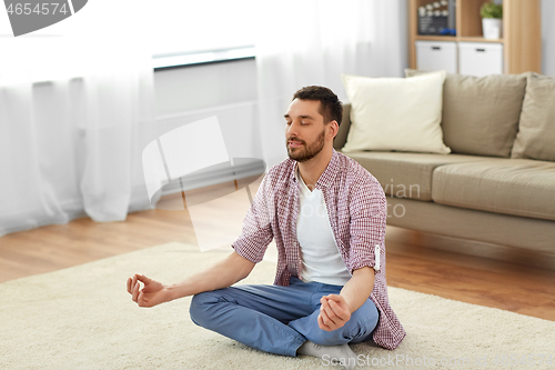 Image of man meditating in lotus pose at home