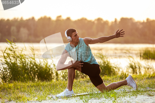 Image of A young athletic man working out listening to the music at the riverside outdoors