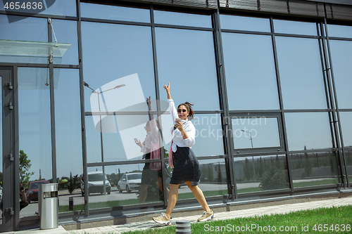 Image of Young woman walking against glass\' wall in airport, traveler with small baggage, influencer\'s lifestyle